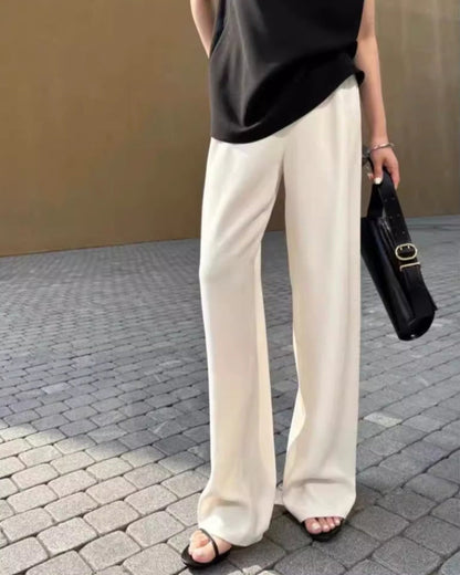 Women's ivory wide-leg high-rise trousers with fluid drape fabric, styled with black sandals and handbag on cobblestone street
