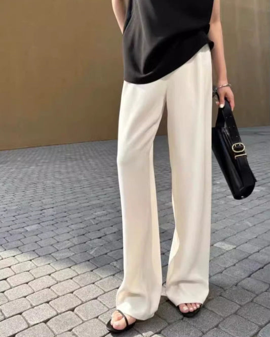 Women's ivory wide-leg high-rise trousers with fluid drape fabric, styled with black sandals and handbag on cobblestone street